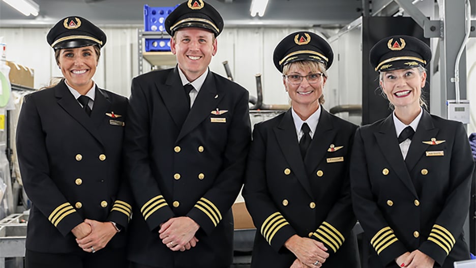 Four Delta pilots standing together in their uniforms posing with smiles