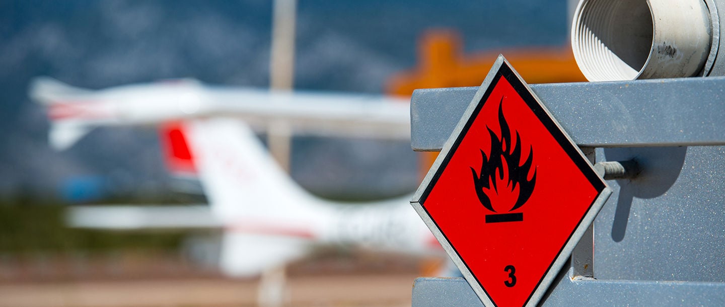 A red flammable warning sign attached to a container of gasoline outside the airport close to the runway