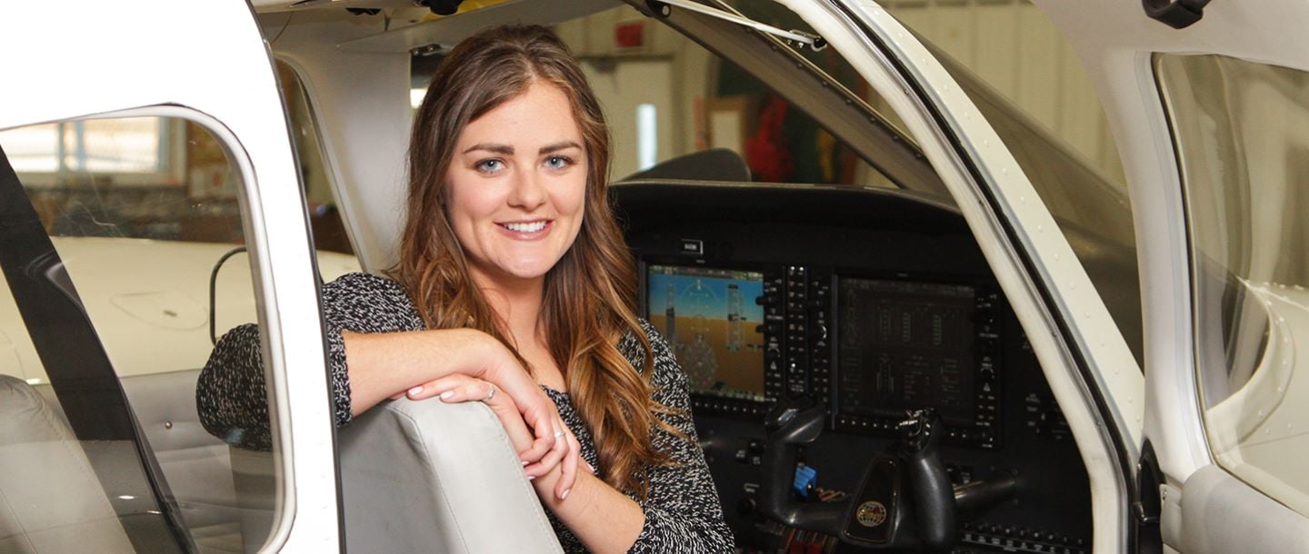 A student sitting in the pilot seat of an airplane posing with a smile