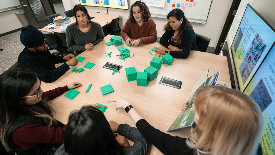 Students at a table in a meeting room using small green building blocks during an elementary training exercise