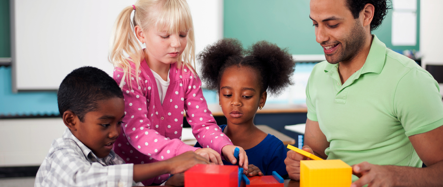 Three elementary students and the teacher sitting at a table in the classroom playing with foam building blocks