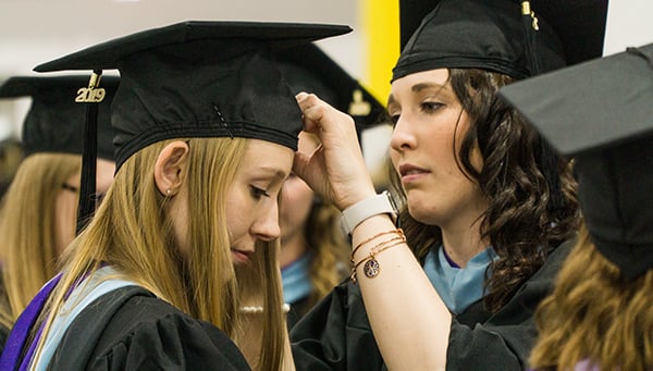 Student helping friend with graduation cap