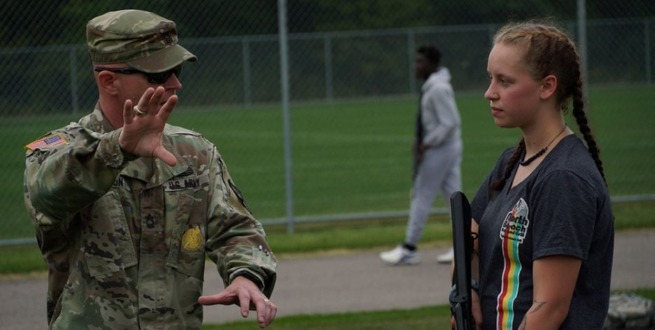An Army Reserve Officers’ Training Corps (ROTC) officer instructing a student outside on the field during training with another student on the track in the background